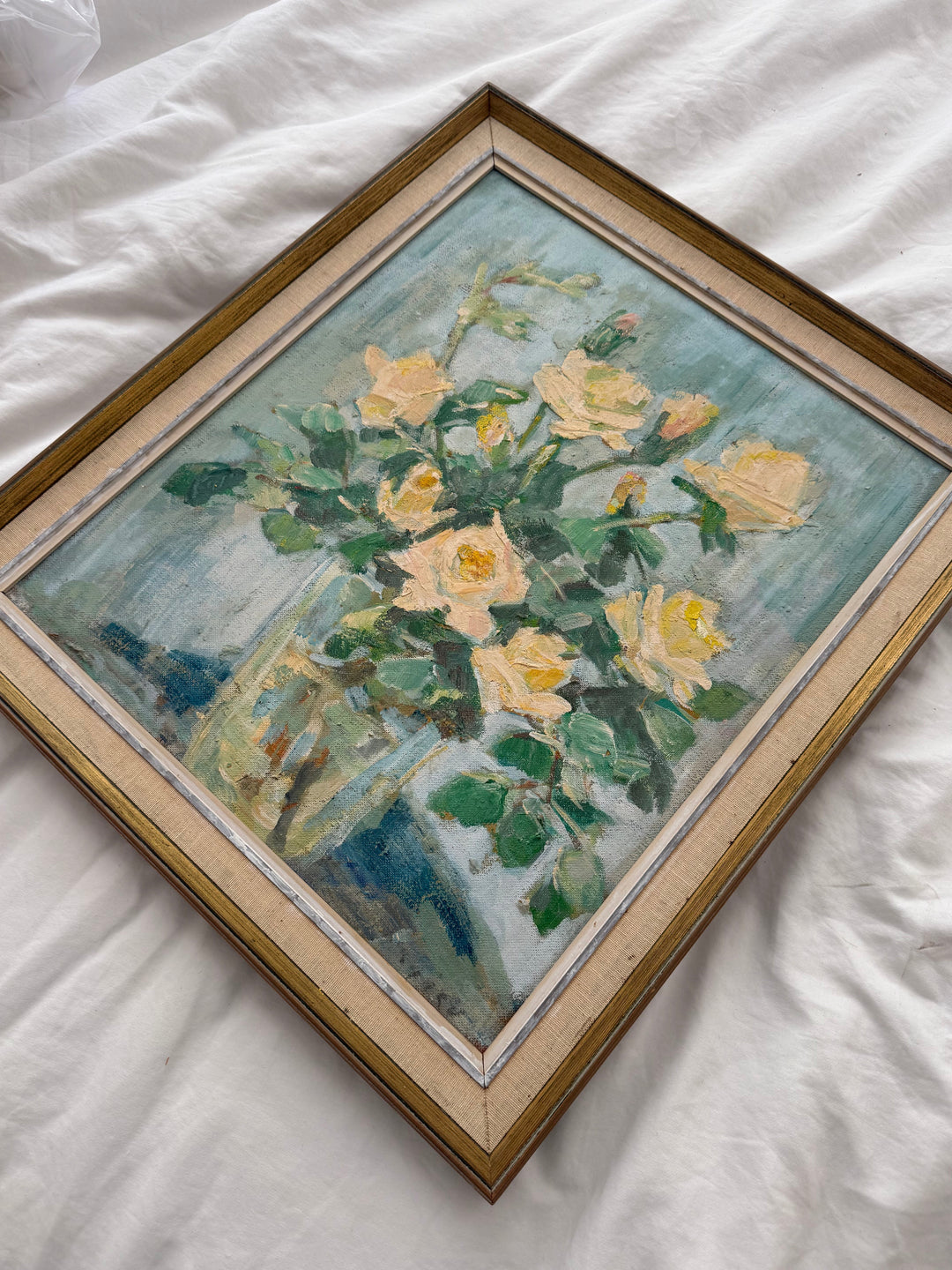 a vintage oil painting of yellow roses with a blue background lying on a white sheet