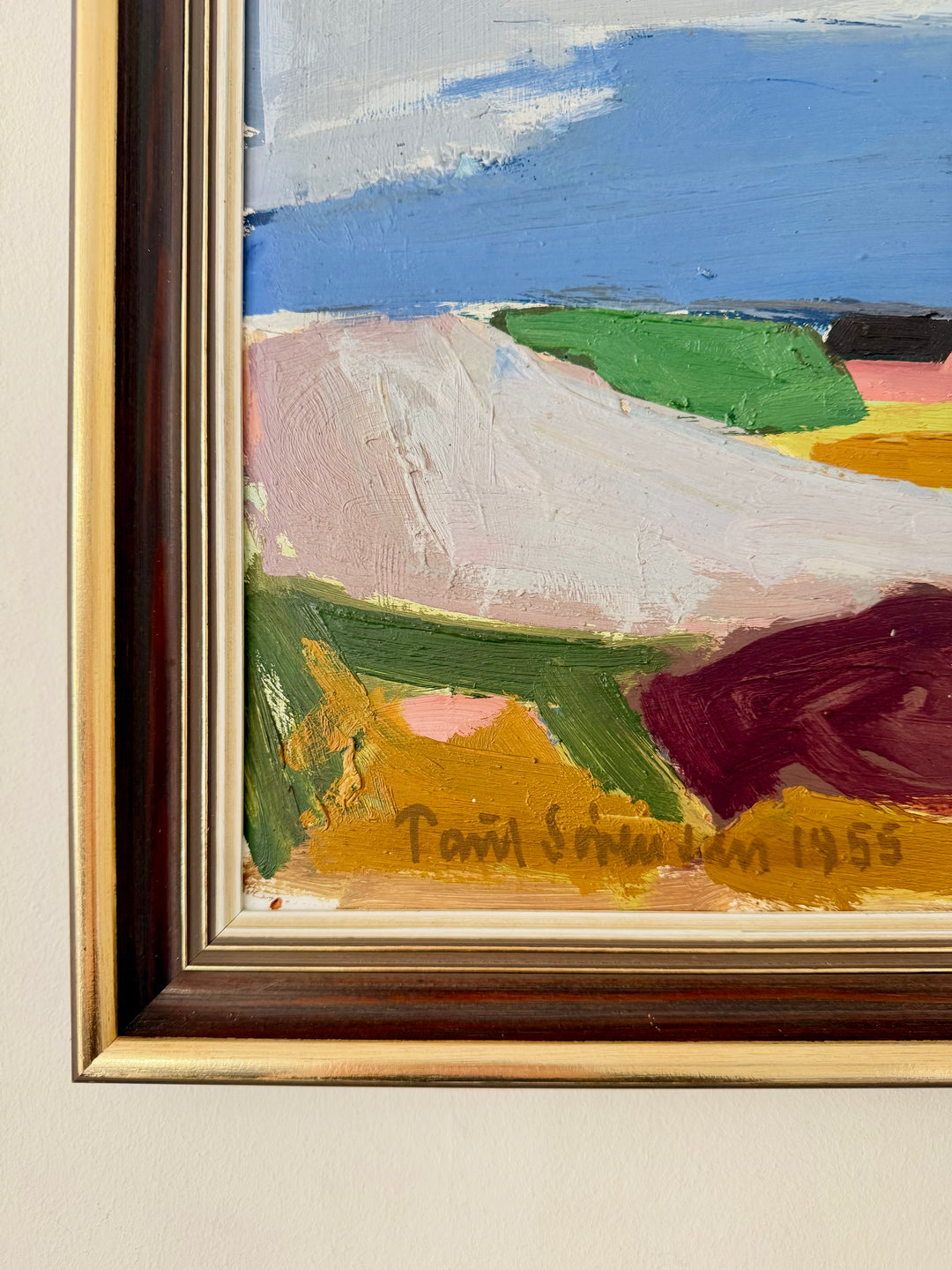 A close-up of a framed abstract landscape painting on a light beige wall. The artwork features thick brushstrokes of blue sky, pale pink, green, yellow, and dark red shapes, with a visible signature reading 'Paul Serre 1955' near the bottom.