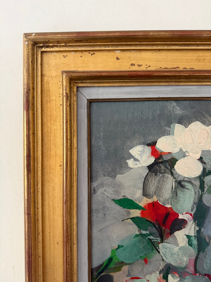 Close-up of a framed painting showing a floral still life with white flowers, green leaves, and a red bloom on a gray background, set in a distressed gold frame.