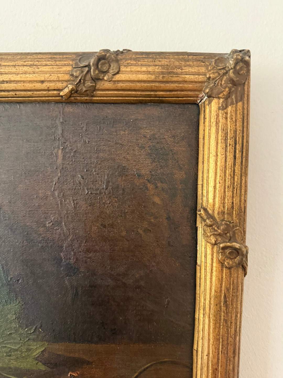 Close-up of an antique-style framed painting showing the ornate gold-toned corner brackets and dark brown painted canvas surface.