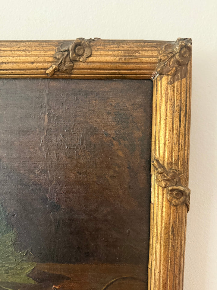 Close-up of an antique-style framed painting showing the ornate gold-toned corner brackets and dark brown painted canvas surface.