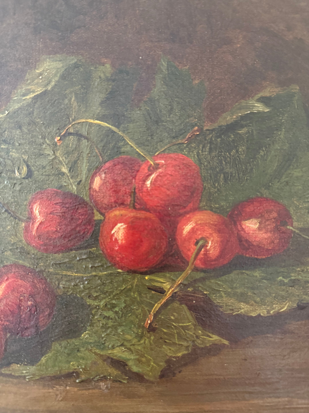 A still life oil painting depicting a cluster of glossy red cherries resting on large green leaves, set against a dark brown background.