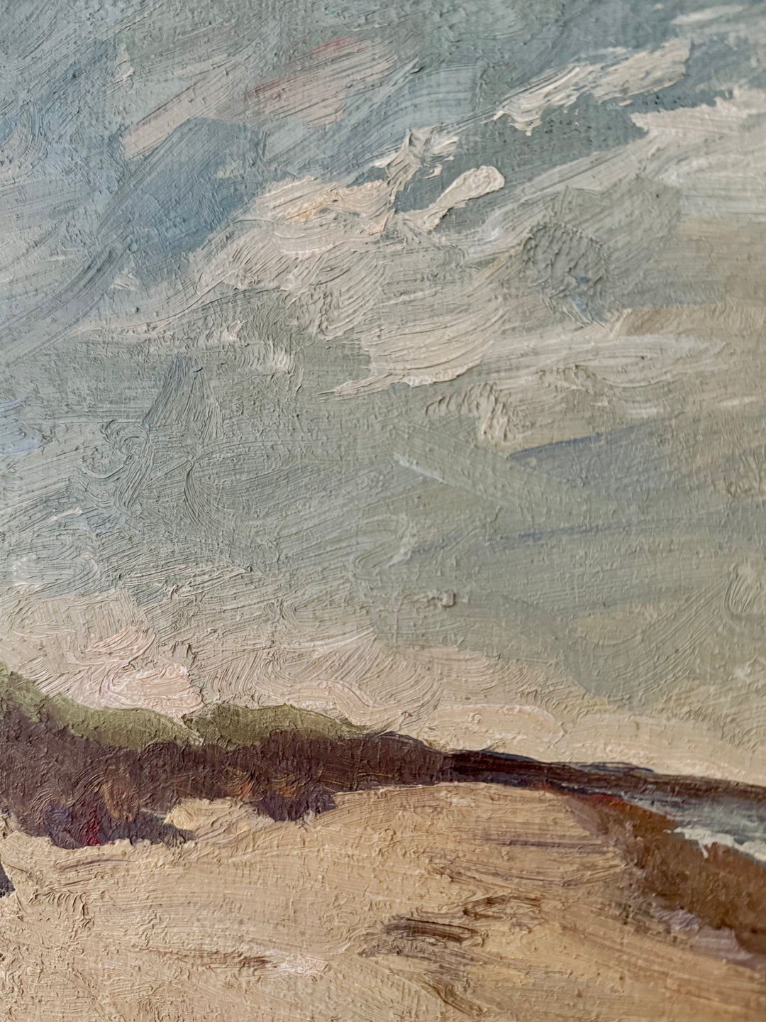 An oil painting detail showing textured brushstrokes of a landscape, featuring a pale blue and gray sky above a sandy beige foreground with dark brown earth.