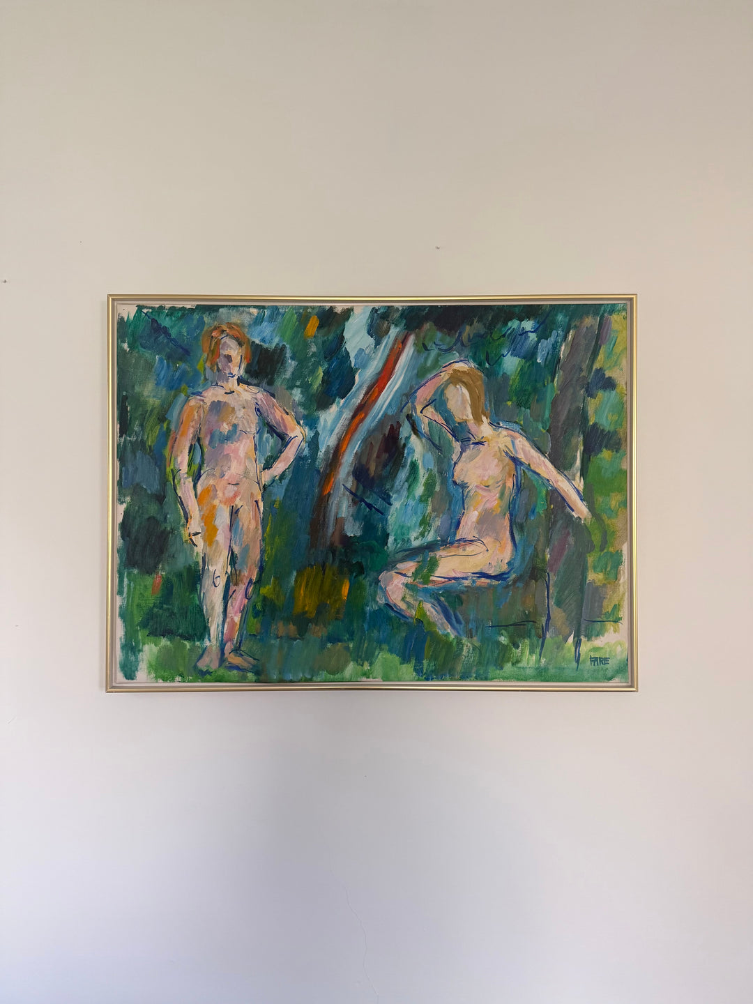 Framed vintage oil painting of two nude figures in a forest setting on a white wall.